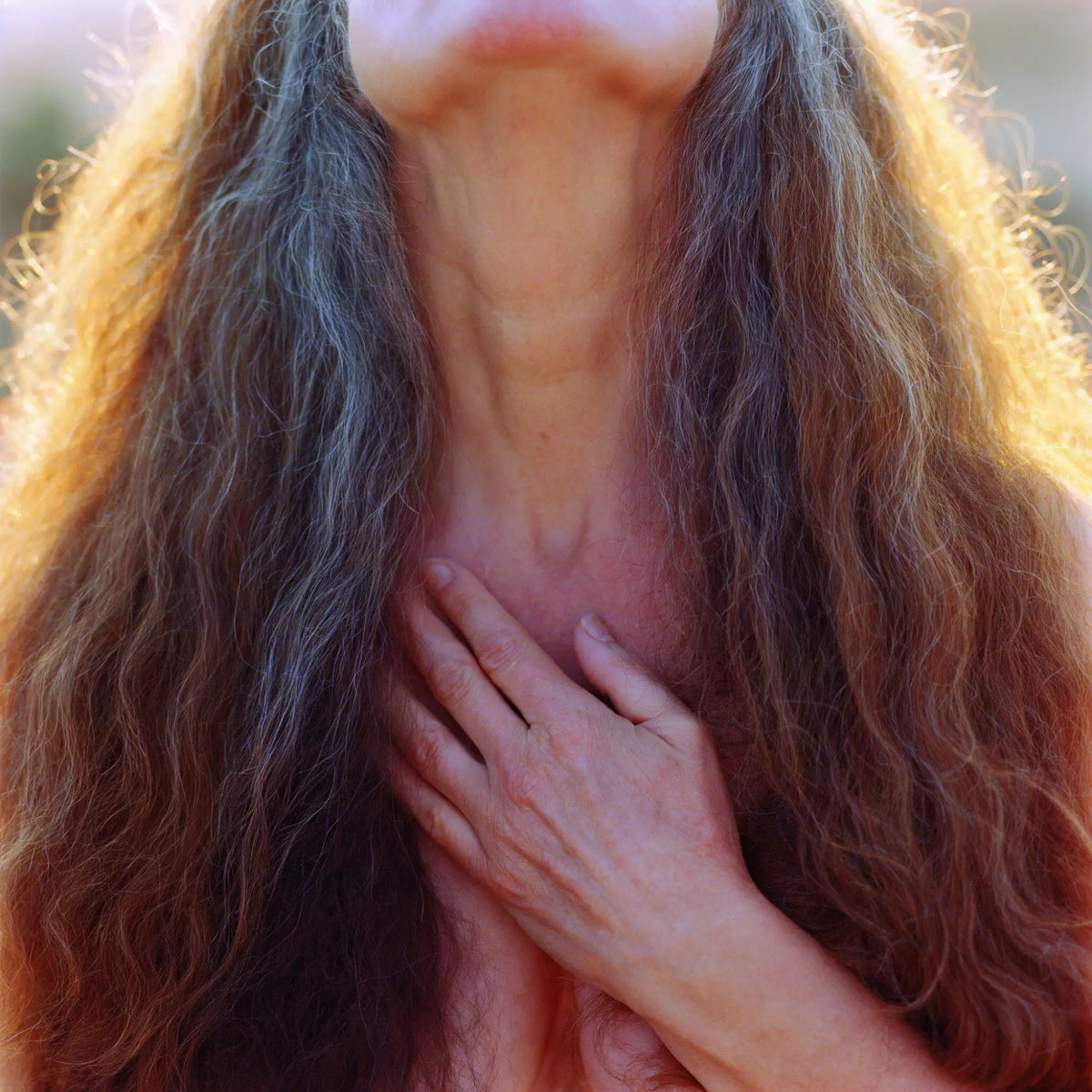 A woman with long wavy hair streaked with silver, one hand resting over her heart